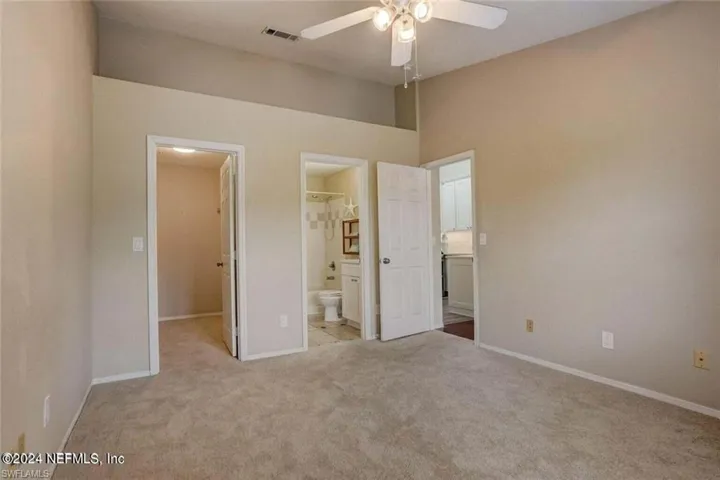 Unfurnished bedroom with a high ceiling, ceiling fan, light colored carpet, a walk in closet, and ensuite bath