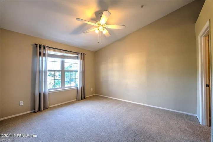 Empty room with ceiling fan, carpet flooring, and vaulted ceiling