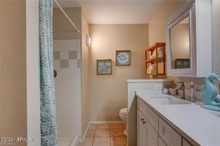 Bathroom featuring a shower with curtain, vanity, tile patterned flooring, and toilet