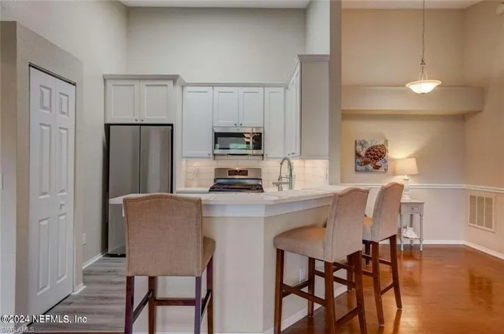 Kitchen with white cabinetry, a breakfast bar area, kitchen peninsula, hardwood / wood-style floors, and appliances with stainless steel finishes