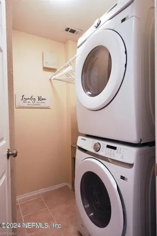 Laundry room featuring stacked washing maching and dryer and tile patterned flooring