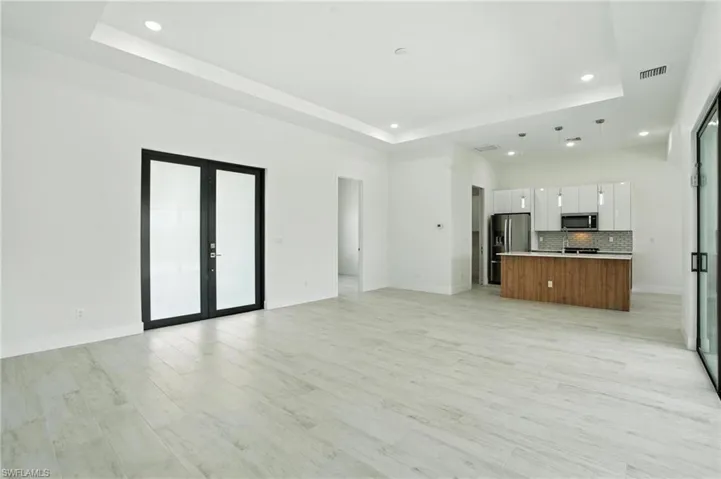 Unfurnished living room with a raised ceiling, recessed lighting, french doors, and light wood-style flooring