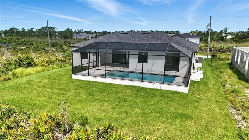 Rear view of house with an outdoor pool, a patio, glass enclosure, and a lawn