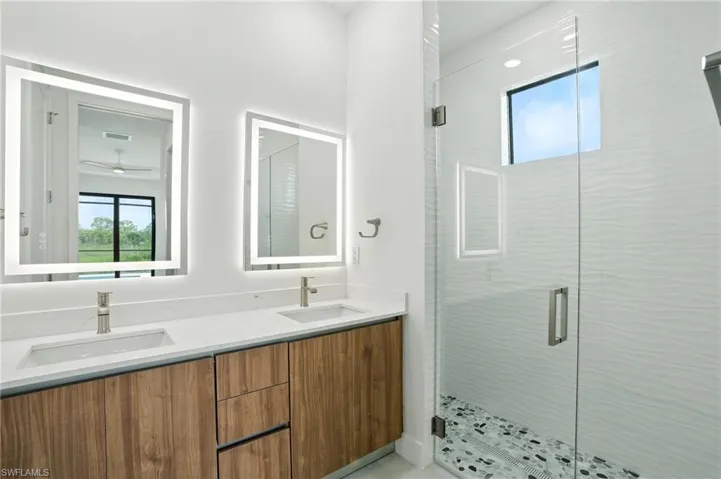 Full bath featuring plenty of natural light, double vanity, a shower stall, and ceiling fan