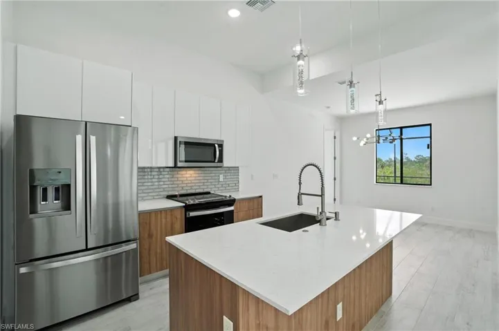 Kitchen with appliances with stainless steel finishes, tasteful backsplash, white cabinetry, pendant lighting, and an island with sink