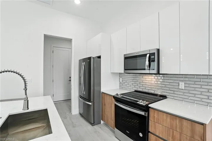 Kitchen with appliances with stainless steel finishes, modern cabinets, white cabinets, backsplash, and light wood-style floors
