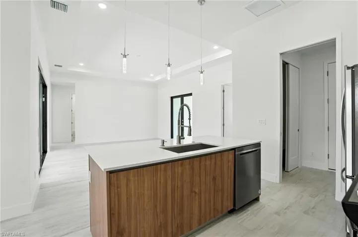 Kitchen with a kitchen island with sink, modern cabinets, recessed lighting, a tray ceiling, and brown cabinetry