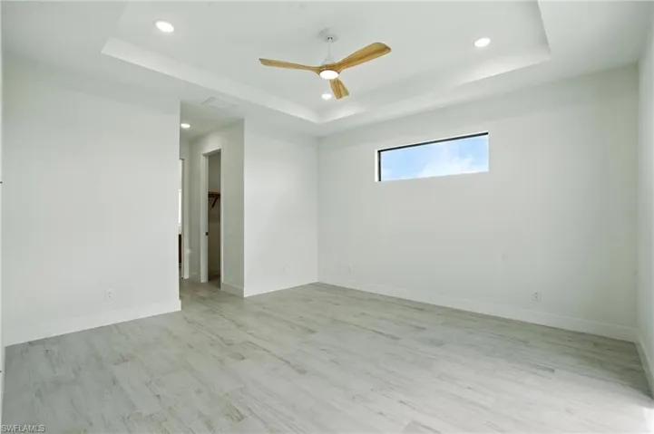 Spare room featuring a raised ceiling, light wood-style flooring, ceiling fan, and recessed lighting