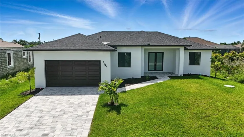 View of front of property featuring a front yard, stucco siding, an attached garage, and decorative driveway