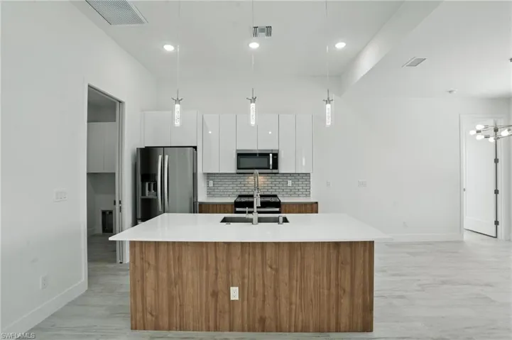 Kitchen with appliances with stainless steel finishes, decorative backsplash, white cabinets, a center island with sink, and decorative light fixtures