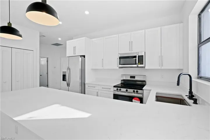 Kitchen with stainless steel appliances, white cabinets, light stone countertops, decorative light fixtures, and a peninsula
