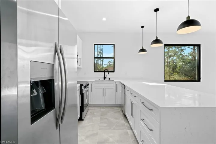 Kitchen with stainless steel appliances, a peninsula, white cabinetry, pendant lighting, and light stone counters