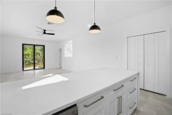 Kitchen with white cabinets, light stone counters, hanging light fixtures, and open floor plan