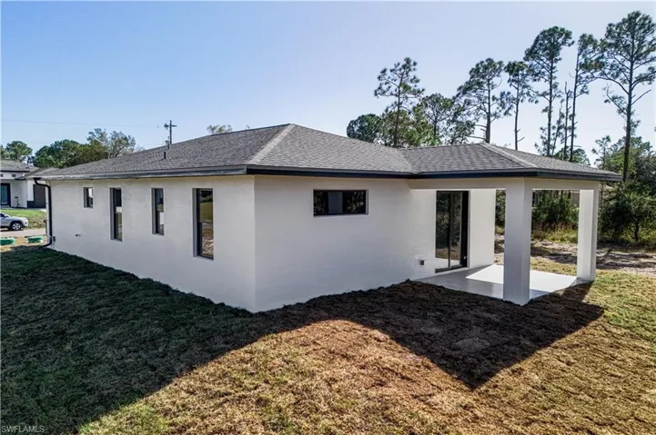 Rear view of property featuring stucco siding, a yard, a patio area, and a shingled roof