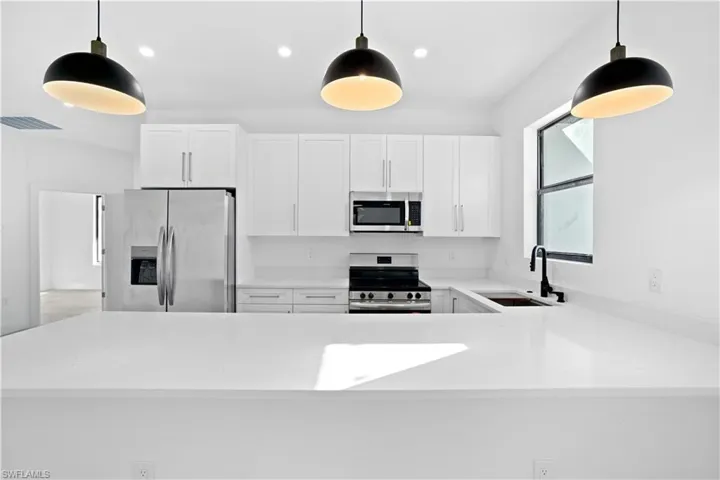 Kitchen with white cabinets, hanging light fixtures, stainless steel appliances, and a peninsula