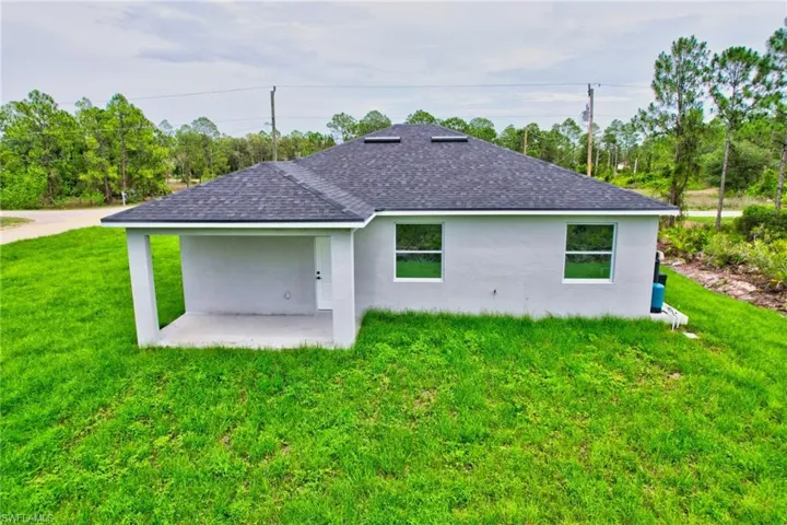 Back of property with roof with shingles, stucco siding, a lawn, and a patio