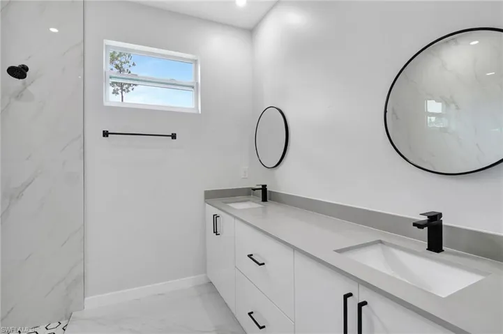 Full bath featuring marble finish flooring, double vanity, baseboards, and a marble finish shower