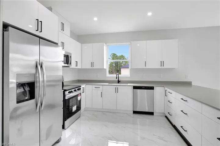 Kitchen with stainless steel appliances, a sink, light marble finish flooring, light countertops, and white cabinets