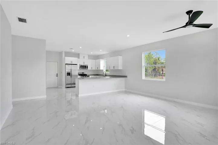 Unfurnished living room featuring light marble finish flooring, baseboards, a ceiling fan, a sink, and recessed lighting