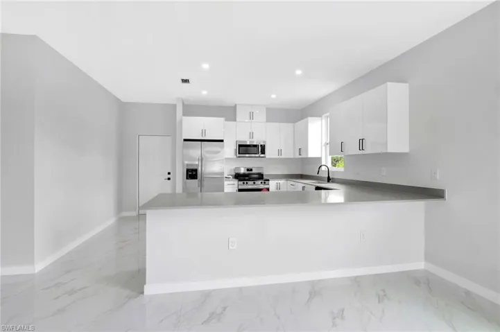 Kitchen featuring stainless steel appliances, light marble finish flooring, baseboards, a peninsula, and recessed lighting