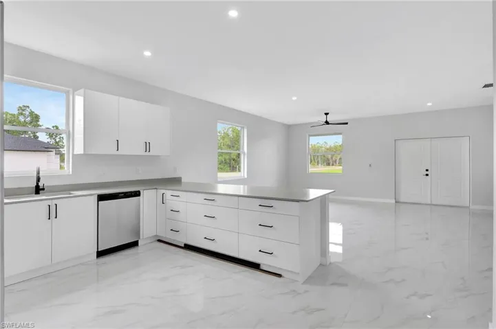 Kitchen with stainless steel dishwasher, a sink, a peninsula, light marble finish flooring, and ceiling fan