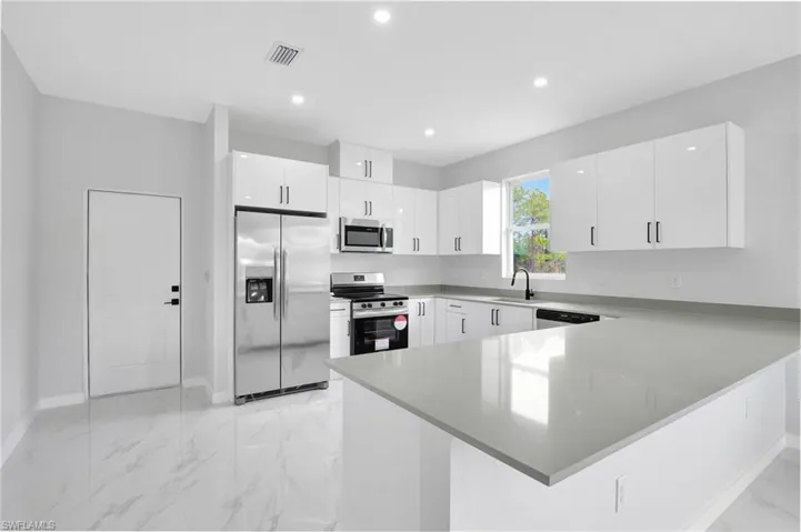 Kitchen featuring stainless steel appliances, a sink, a peninsula, baseboards, and white cabinets
