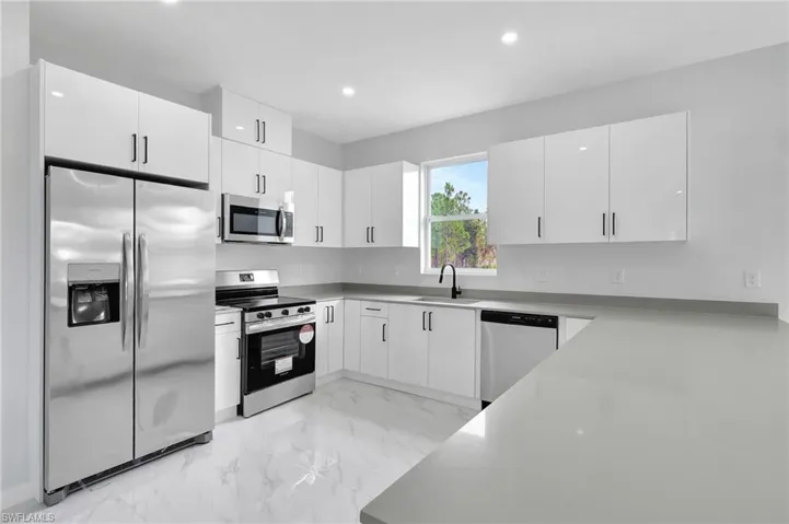 Kitchen featuring appliances with stainless steel finishes, a sink, light marble finish flooring, white cabinetry, and recessed lighting