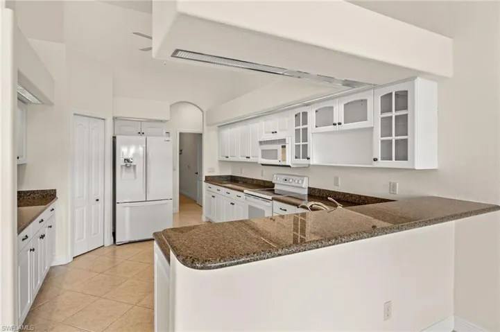 Kitchen featuring white appliances, glass fronted cabinets, white cabinetry, a peninsula, and light tile patterned floors