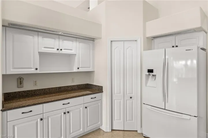Kitchen with white refrigerator with ice dispenser, white cabinets, dark stone countertops, and light tile patterned floors