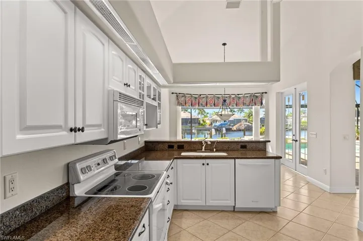 Kitchen featuring white appliances, a peninsula, white cabinetry, glass insert cabinets, and french doors