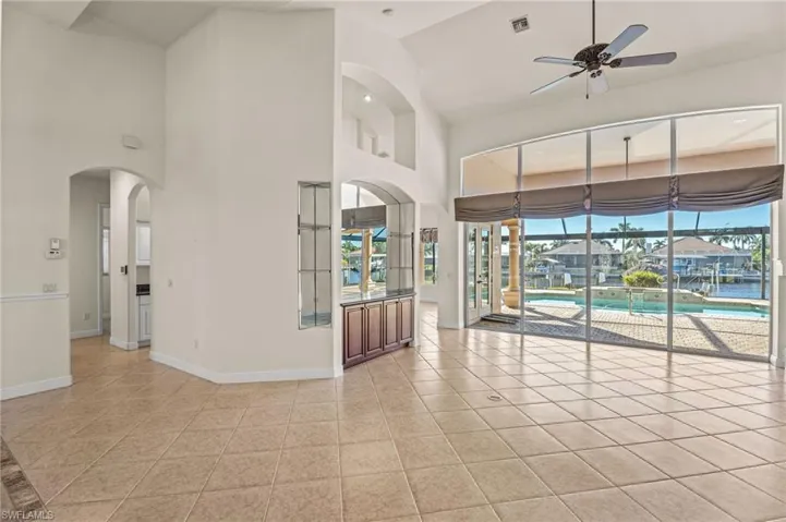 Spare room featuring a ceiling fan, light tile patterned floors, arched walkways, a sunroom, and vaulted ceiling