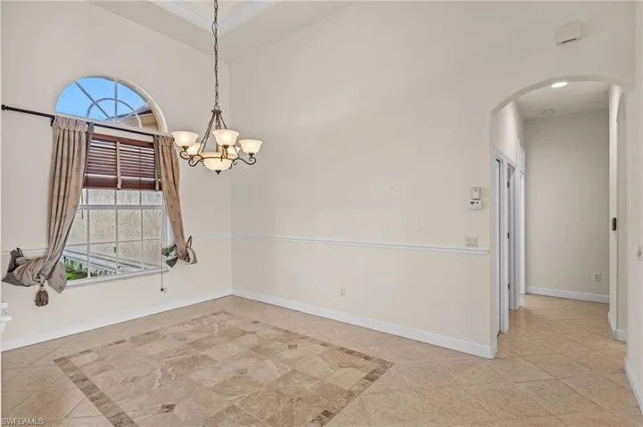 Spare room with arched walkways, a high ceiling, inlaid floor details, and a chandelier