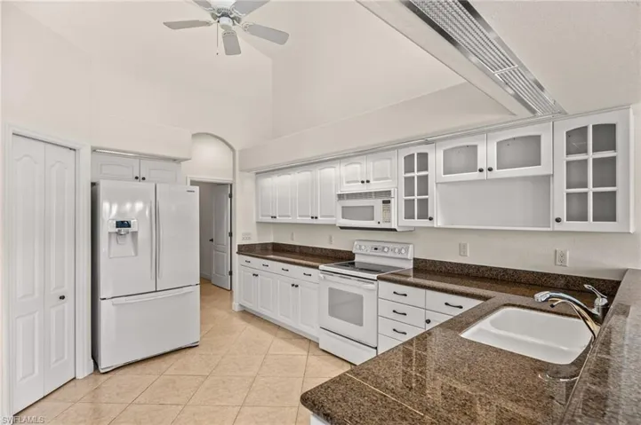 Kitchen with white appliances, dark countertops, glass insert cabinets, white cabinets, and a high ceiling