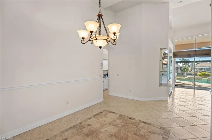 Empty room with arched walkways, inlaid floor details, hanging lights, a high ceiling, and light tile patterned flooring