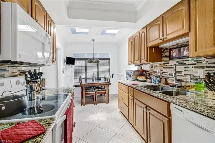 Kitchen with light tile patterned flooring, light stone counters, white appliances, a skylight, and sink