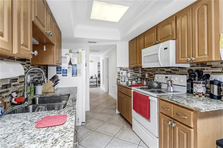 Kitchen featuring white appliances, light stone countertops, light tile patterned floors, ornamental molding, and sink