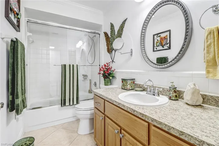 Full bathroom featuring combined bath / shower with glass door, tile patterned floors, ornamental molding, vanity, and toilet
