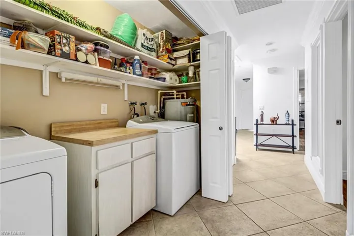 Clothes washing area featuring cabinets, light tile patterned floors, electric water heater, and washer and clothes dryer