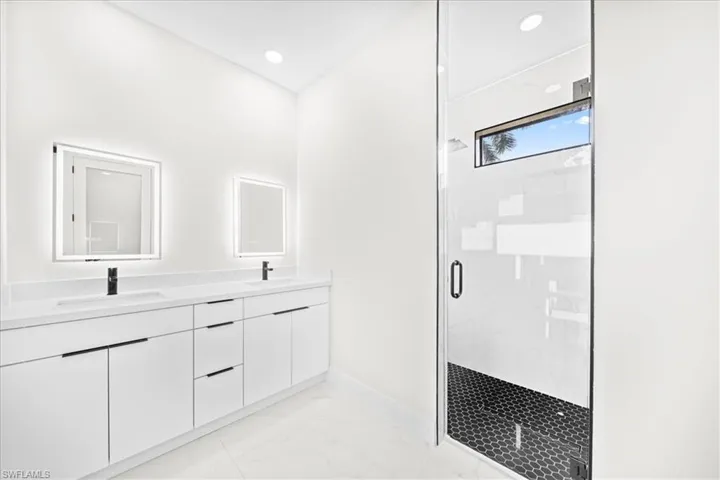 Bathroom featuring a marble finish shower, double vanity, light marble finish floors, and recessed lighting