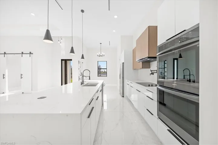 Kitchen with modern cabinets, stainless steel appliances, a large island, light stone countertops, and white cabinets