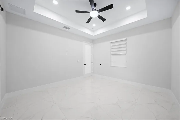 Empty room featuring recessed lighting, light marble finish flooring, ceiling fan, and a raised ceiling