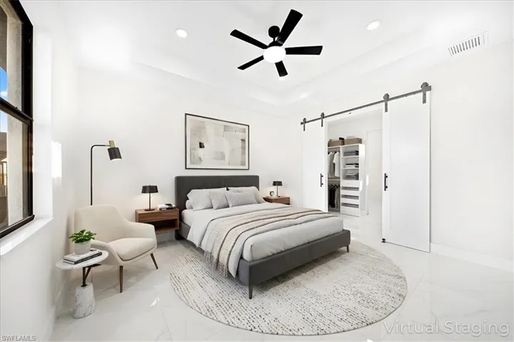Bedroom featuring a barn door, a raised ceiling, a spacious closet, ceiling fan, and recessed lighting
