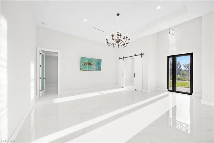 Hall featuring a barn door, a chandelier, light marble finish flooring, and a high tray ceiling