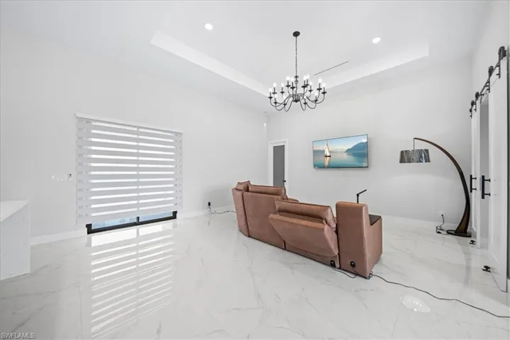 Living area with a barn door, light marble finish flooring, hanging lights, and a raised ceiling