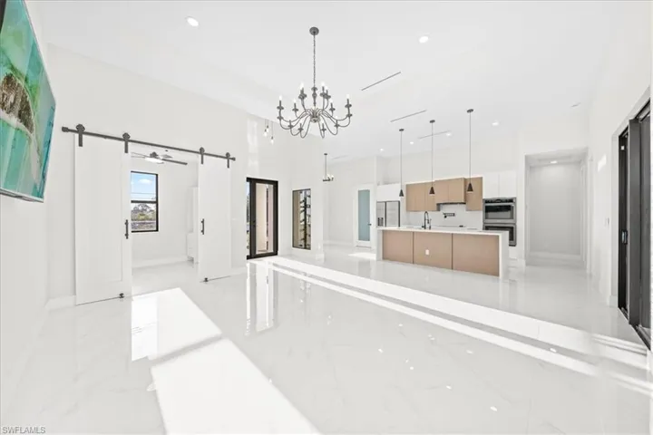 Kitchen featuring suspended lighting, a barn door, open floor plan, light marble finish floors, and modern cabinets