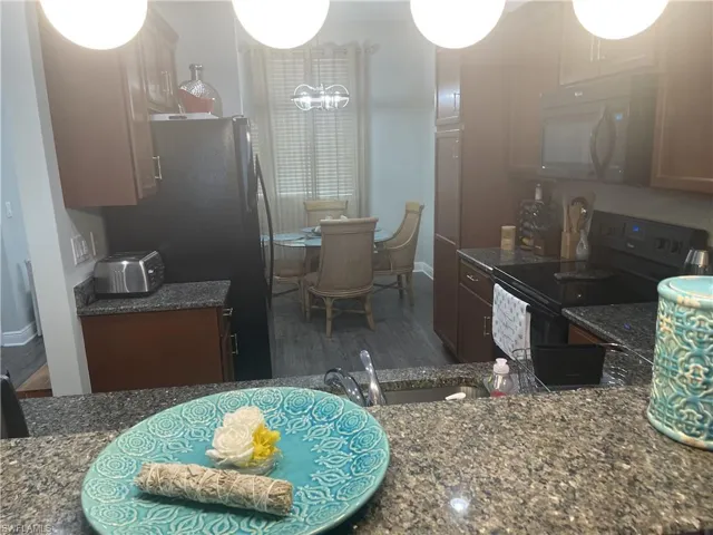 Kitchen featuring black electric range, white microwave, wood finished floors, and dark stone counters