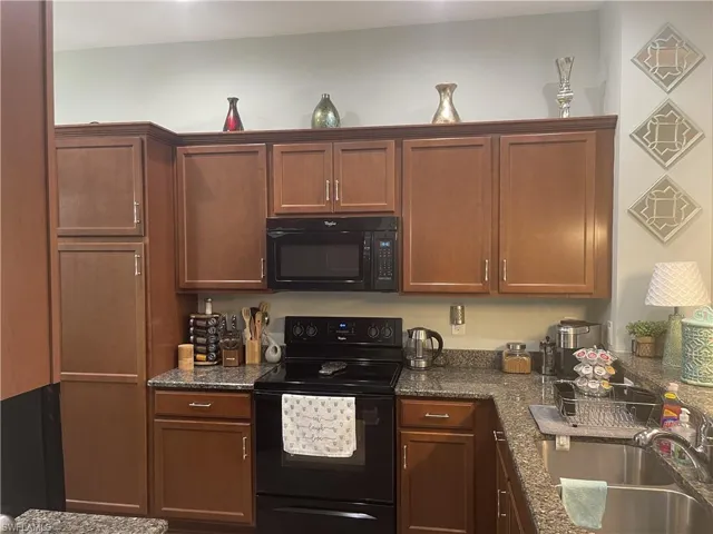Kitchen featuring black appliances, dark stone countertops, and wood finish cabinetry