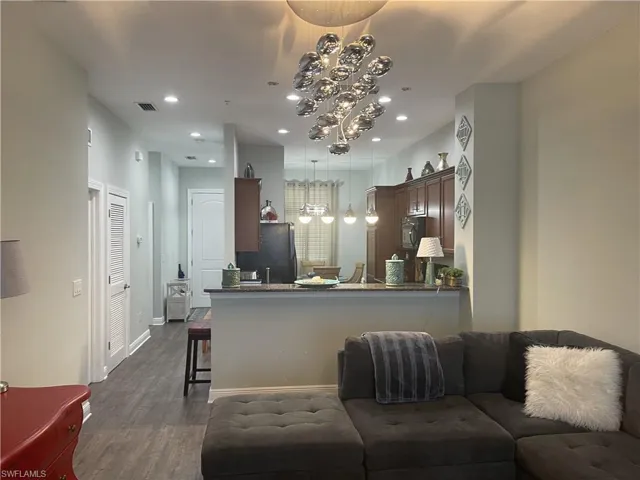 Kitchen featuring open floor plan, a peninsula, dark stone counters, dark wood finished floors, and hanging lights