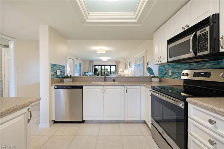 Kitchen with stainless steel appliances, white cabinets, decorative backsplash, and light tile patterned floors.
