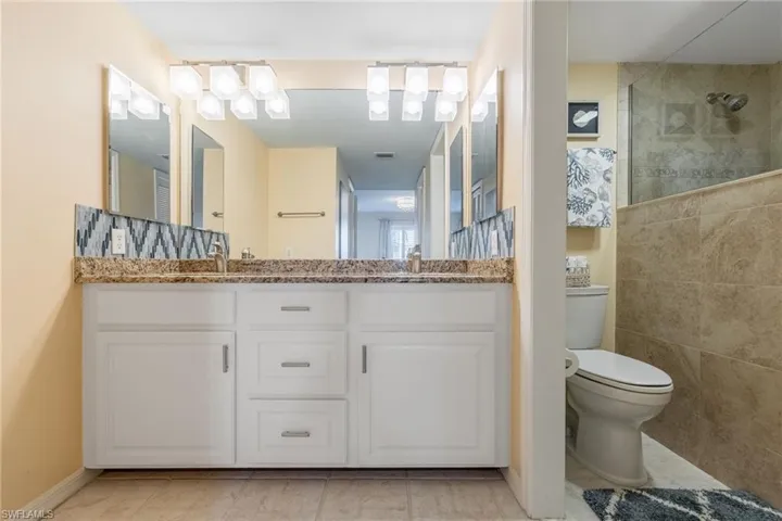 Bathroom featuring double vanity with granite counter, a walk-in tile shower.